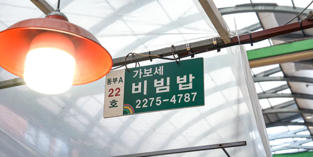 Green stall sign reading Gabose Bibimbap with stall number Dongbu A-22 and phone number 2275-4787, hanging inside Gwangjang Market