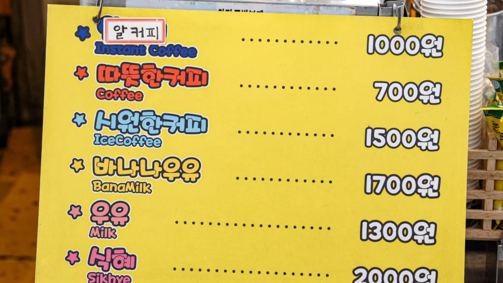Gwangjang Toast drink menu board listing instant coffee ₩1,000, hot coffee ₩700, iced coffee ₩1,500, banana milk ₩1,700, milk ₩1,300, and sikhye ₩2,000.