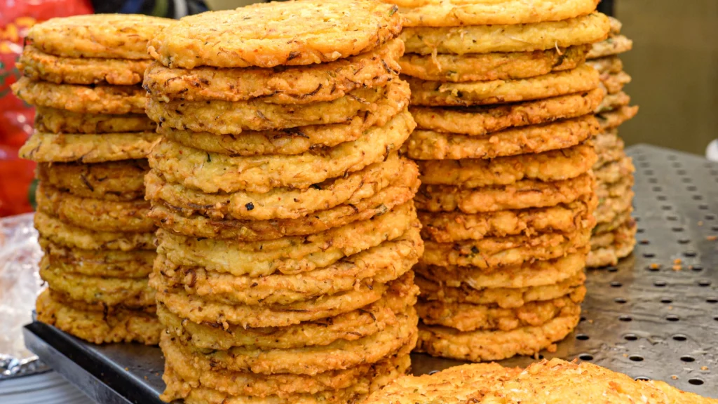 Tall stacks of freshly made bindaetteok (Korean mung bean pancakes) piled up at a Gwangjang Market vendor stall — one of the market's most iconic street foods to enjoy alongside a visit to Gangga-ne Tteokbokki.