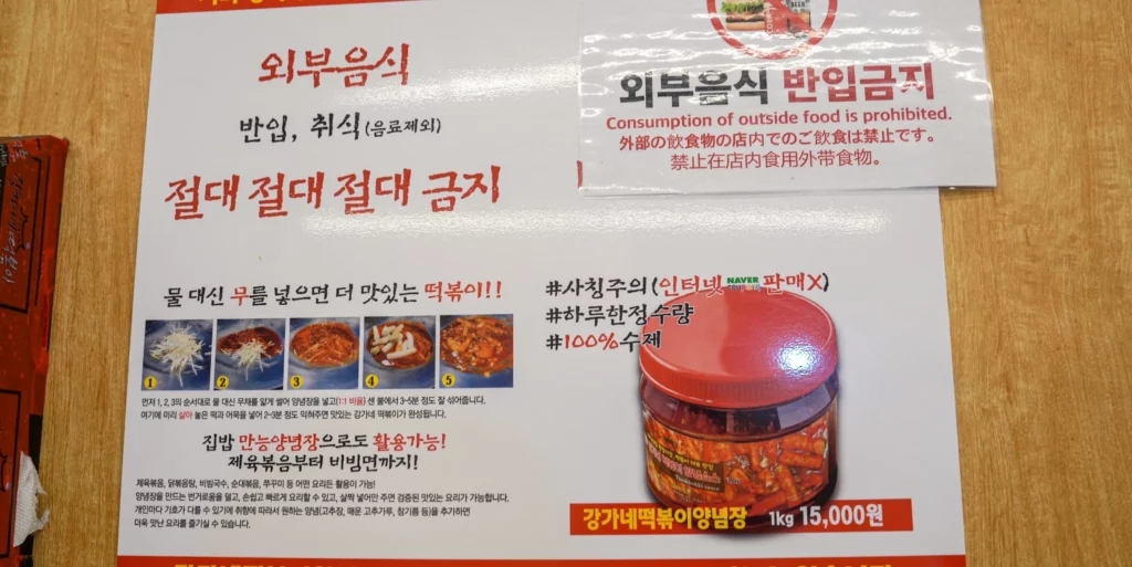 Gangga-ne Tteokbokki in-store notice displaying a no-outside-food policy in four languages, a five-step radish tteokbokki cooking guide, and the take-home tteokbokki sauce jar priced at 1kg 15,000won.<br>