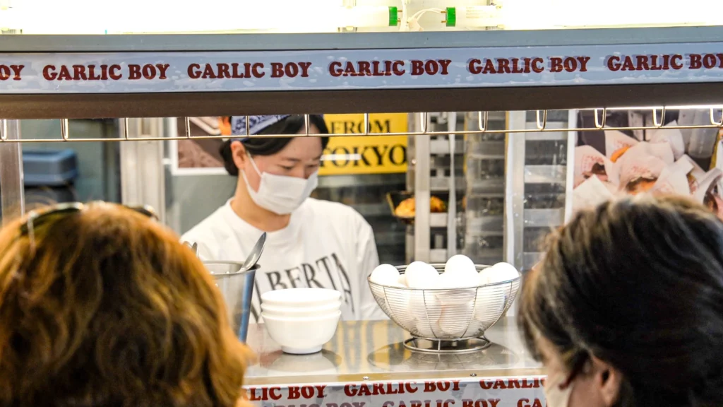 A Garlic Boy staff member behind the counter serving customers, with the repeated 