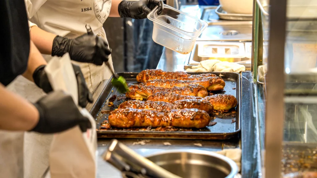 A Garlic Boy staff member in black gloves handling freshly baked garlic butter bread on a baking tray inside the stall kitchen.