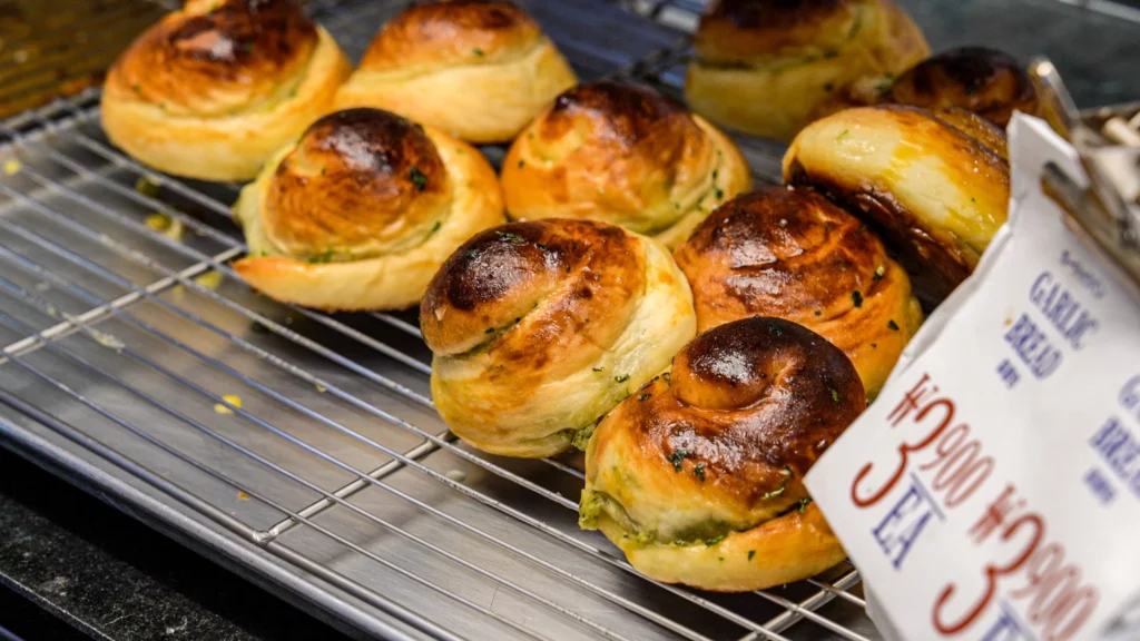 Golden-brown Korean garlic bread buns fresh from the oven arranged on a wire cooling rack, with a price sign reading 