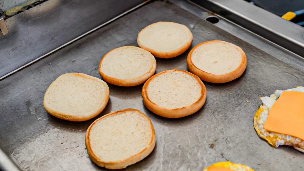 Burger buns toasting on a flat iron griddle alongside a fried egg topped with cheese at Samdeok Burger.
