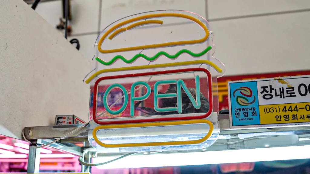 Neon OPEN sign shaped like a burger hanging at the Samdeok Burger stall inside Anyang Jungang Market.
