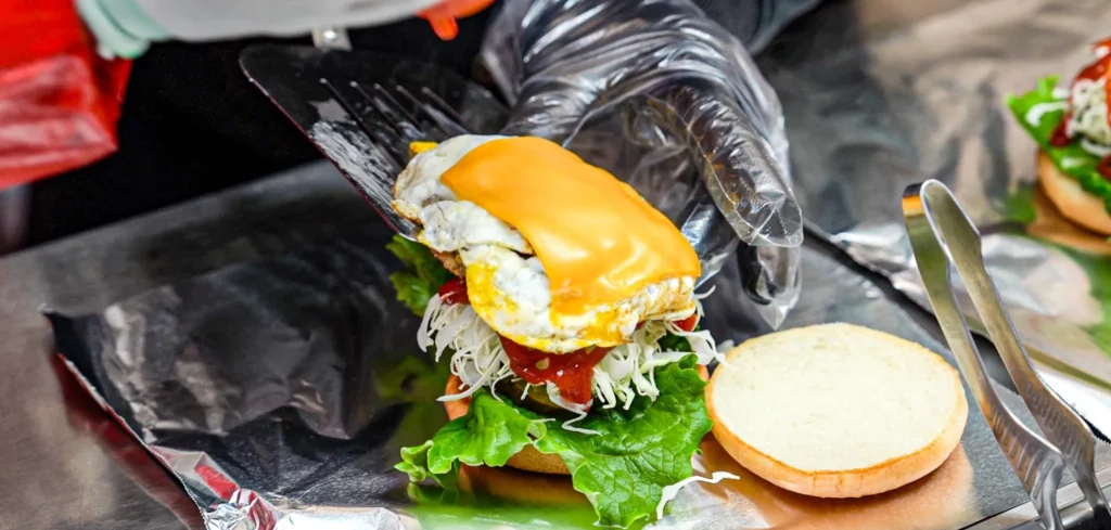 Spatula placing a melted cheese-covered fried egg onto the bulgogi burger assembly at Samdeok Burger stall