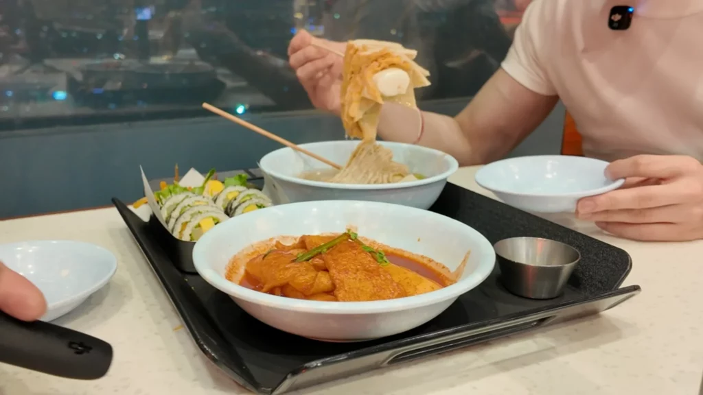 Customer enjoying eomuk and tteokbokki at Durumi Bunsik with Seoul city night view in background