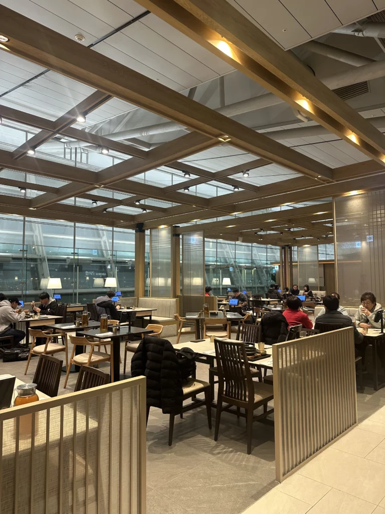 A wide view of the bustling dining area in an Incheon Airport Korean restaurant, showing travelers enjoying their meals in a warm, wood-accented setting.