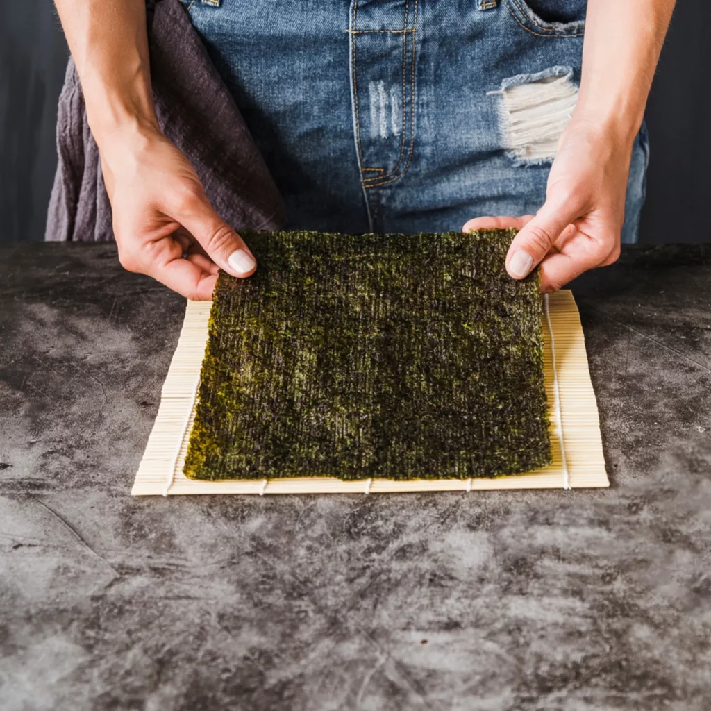 Chef placing dried seaweed sheet on bamboo mat for rolling Durumi Bunsik-style kimbap