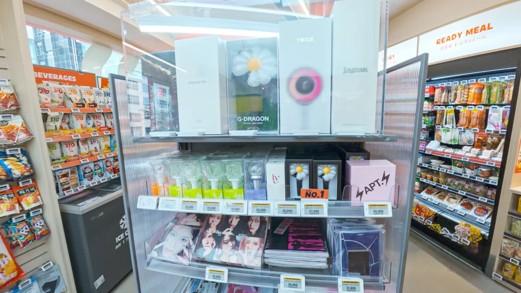 K-pop merchandise display with official lightsticks from G-Dragon, TWICE, Jay Park, IVE, and aespa alongside idol albums.
