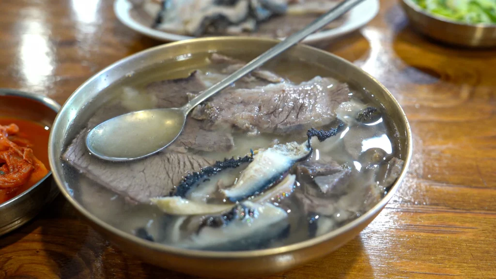 Hadongkwan's Hanwoo gomtang served in a brass bangjja yugi bowl with clear amber broth, brisket slices, and tripe.
