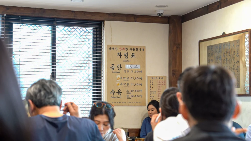 Hadongkwan Myeongdong dining room with the wooden menu board listing gomtang, 25-gong, 30-gong, and suyuk prices.

