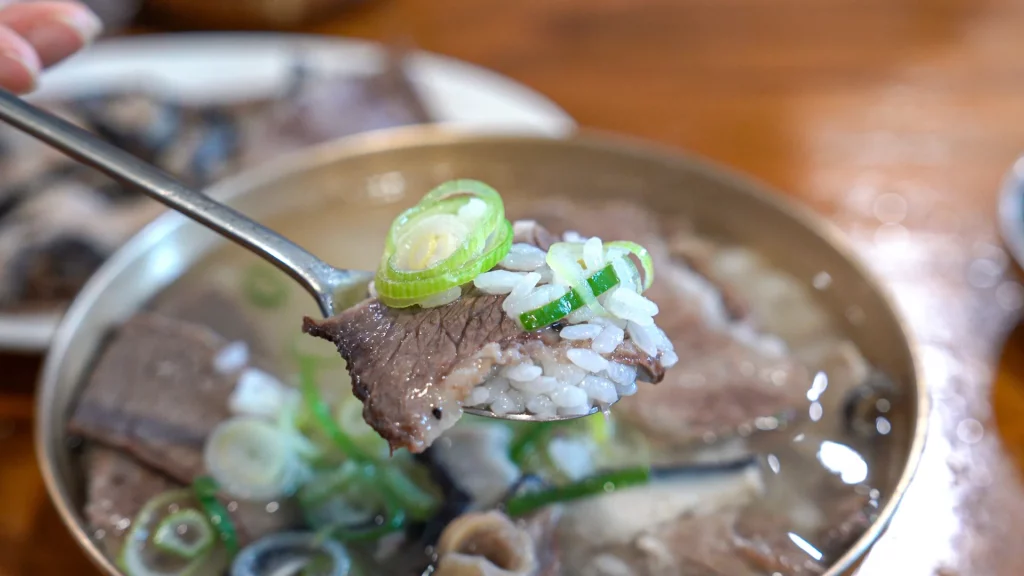 Spoonful of broth-soaked rice topped with Hanwoo brisket and freshly sliced daepa green onion from a Hadongkwan gomtang bowl.