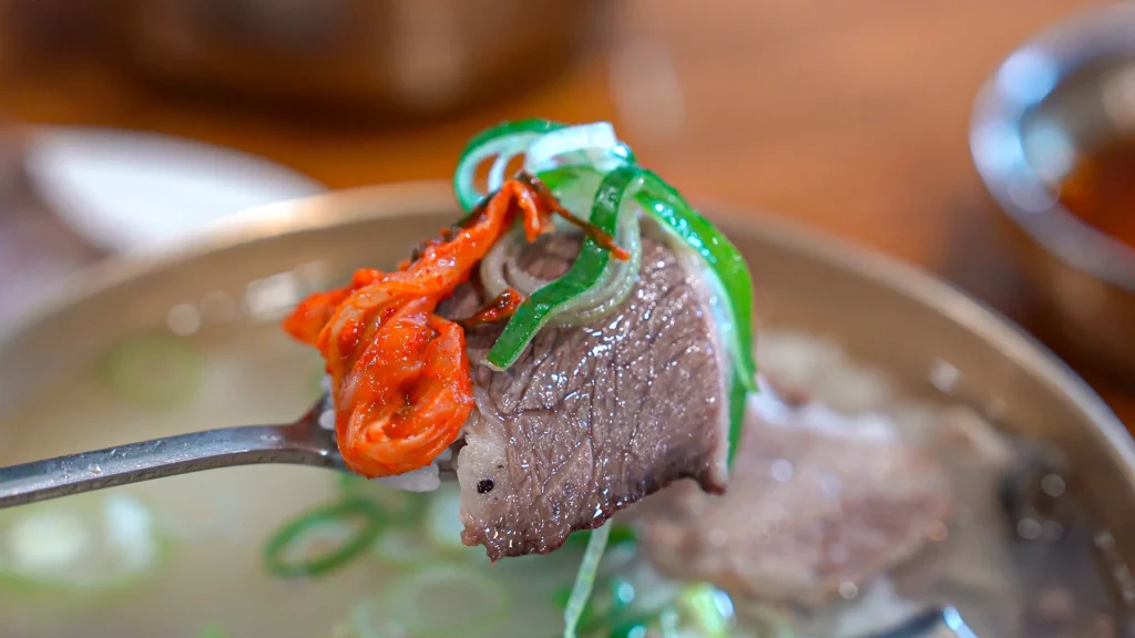 A spoonful combining Hanwoo brisket, kkakdugi radish kimchi, and chopped daepa — the local kkak-guk eating method.
