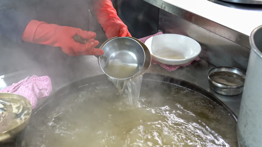 Hadongkwan's broth-master pouring clear Hanwoo broth back into the simmering pot during the toryeom warming process