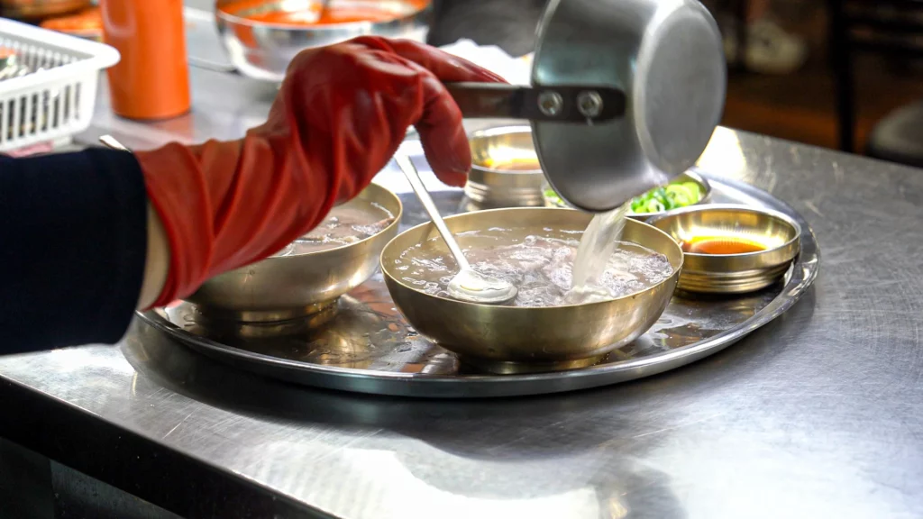 Hadongkwan's broth-master pouring clear Hanwoo broth back into the simmering pot during the toryeom warming process.