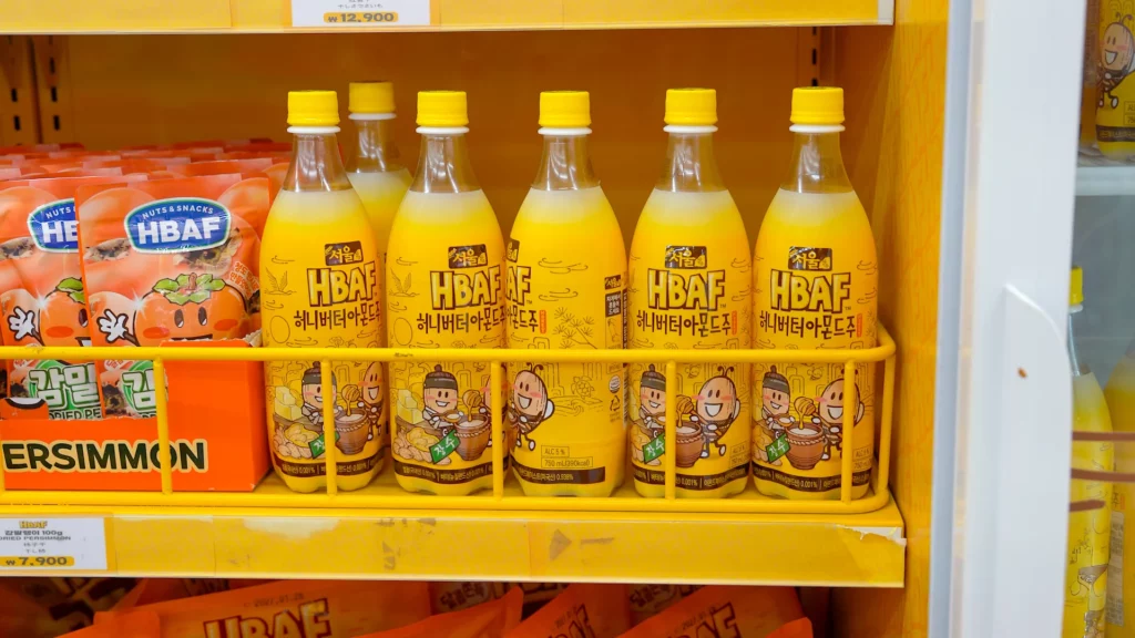 Row of HBAF Honey Butter Almond Makgeolli 750ml bottles with yellow caps chilling on the store's refrigerator shelf.
