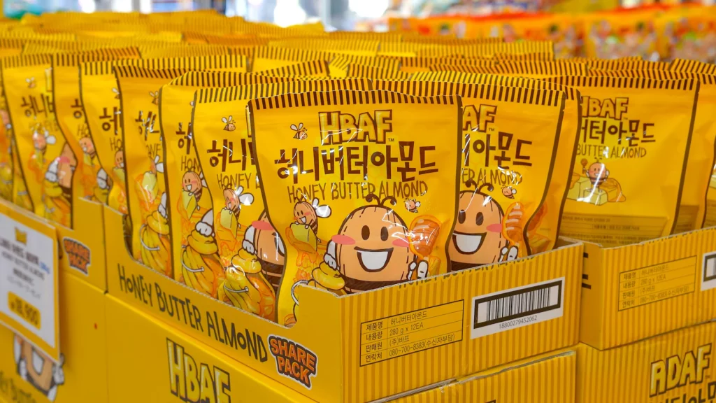 Rows of HBAF Honey Butter Almond share pack pouches stacked in yellow display boxes at HBAF Almond Store Myeongdong.