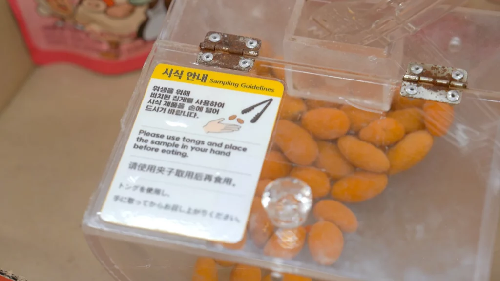 Acrylic sampling box filled with orange-coated almonds and multilingual tasting guidelines at HBAF Almond Store Myeongdong.