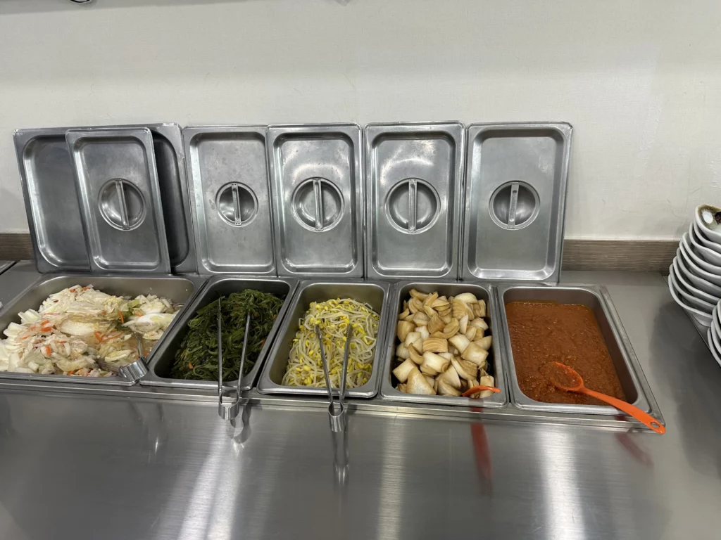 Self-serve banchan bar with white kimchi, seaweed, bean sprouts, pickled radish, and ssamjang at this BTS favorite Jeju restaurant.