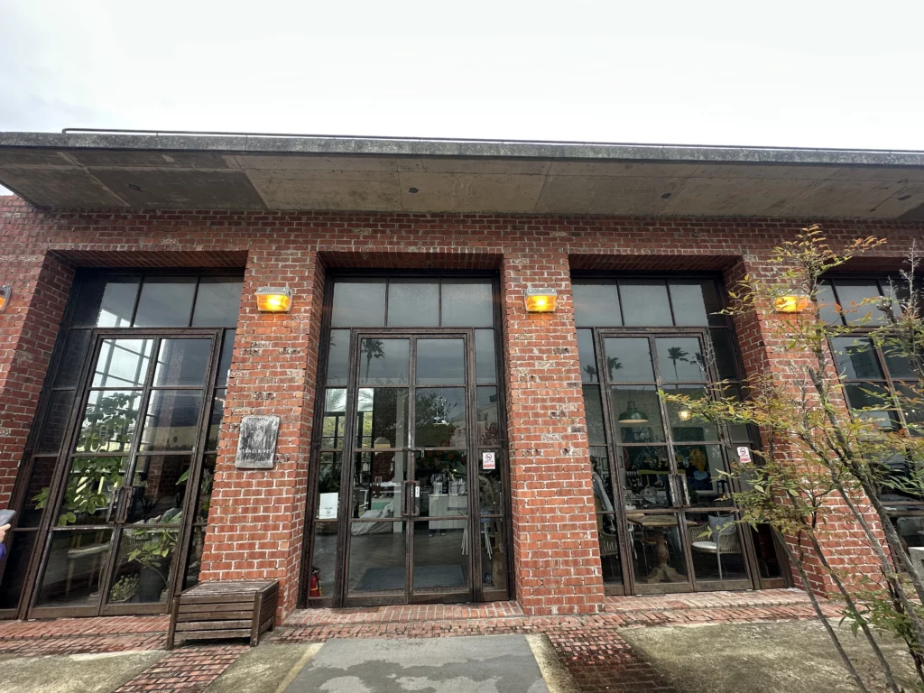 Exterior of jeju brunch cafe Tangerine, a converted red brick warehouse with lawn and garden trees in Seogwipo.