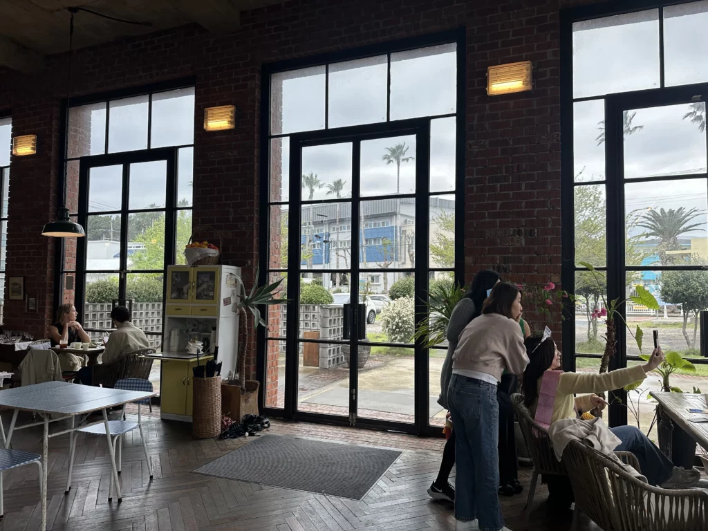 Interior of jeju brunch cafe Tangerine with red brick walls, tall industrial windows, and guests near the entrance.