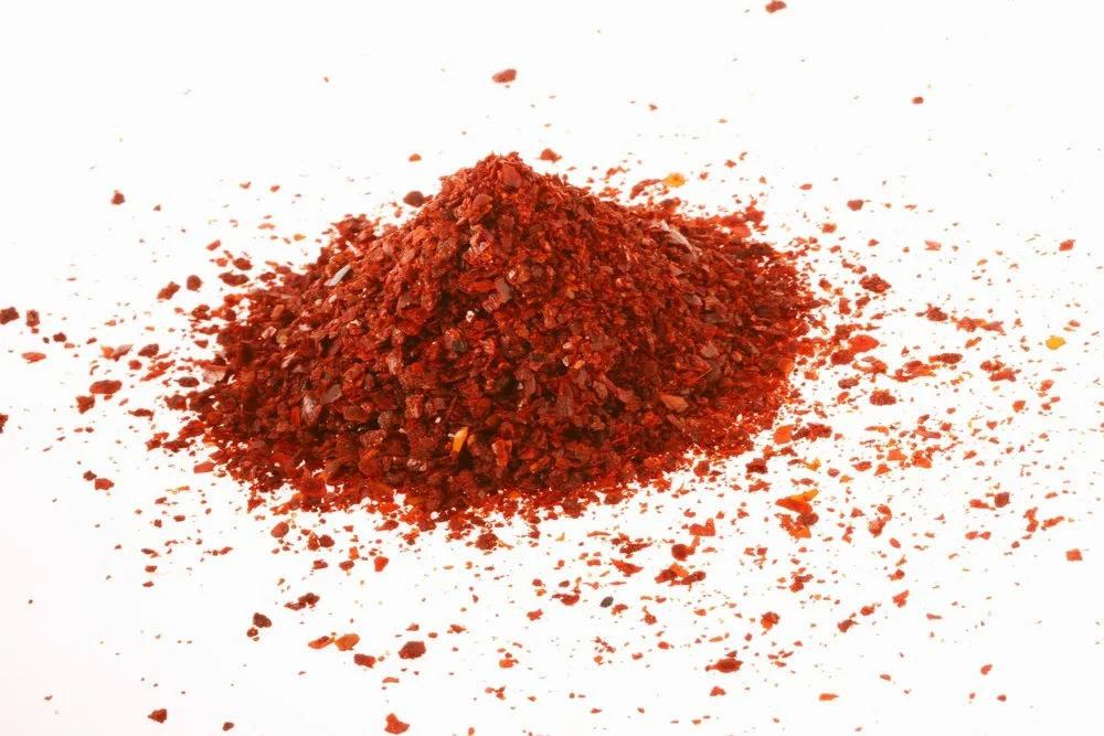 A mound of gochugaru (Korean red pepper flakes) on a white background, the key spice ingredient behind the heat and colour of Korean ramyun broth.