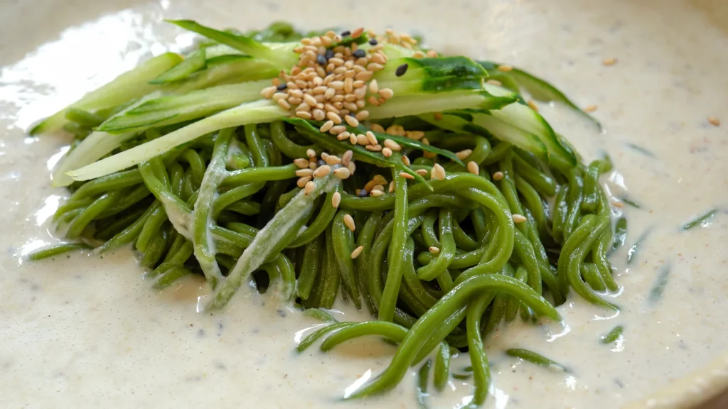 Kongguksu with chilled chlorella-tinted green noodles in cold soybean broth topped with cucumber and sesame seeds.
