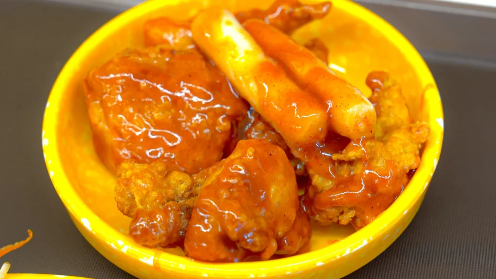 Spicy Korean dak-gangjeong with tteokbokki rice cakes served in chickgimbap's signature yellow bowl