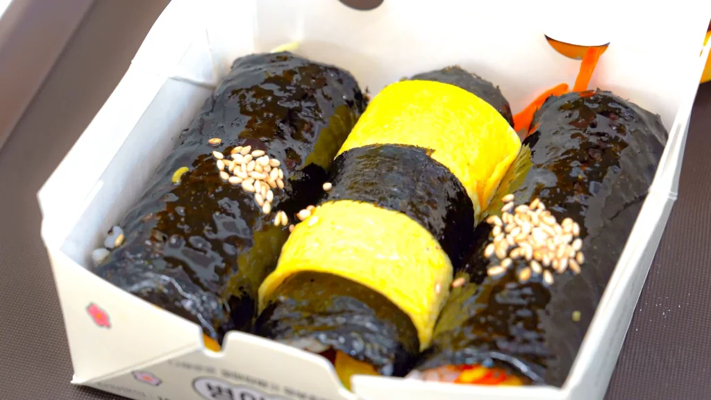 Three chickgimbap mini gimbap rolls packed in a chick-printed dosirak box, perfect for a Myeongdong hotel lunch.