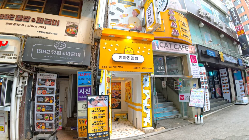 Bright yellow chickgimbap Myeongdong storefront tucked into a Myeongdong alleyway between local shops and a cat café.