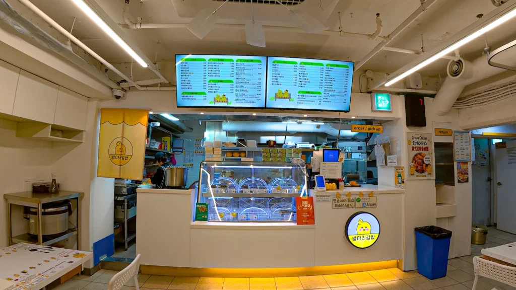 chickgimbap Myeongdong order and pickup counter with digital menu screens, gimbap showcase, and Alipay·WeChat Pay signs.