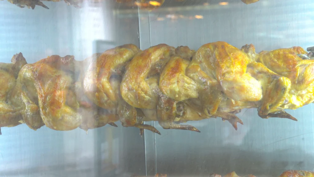 Row of whole chickens slow-roasting on the vertical electric rotisserie behind the Yeongyang Center Myeongdong tongdak display window.