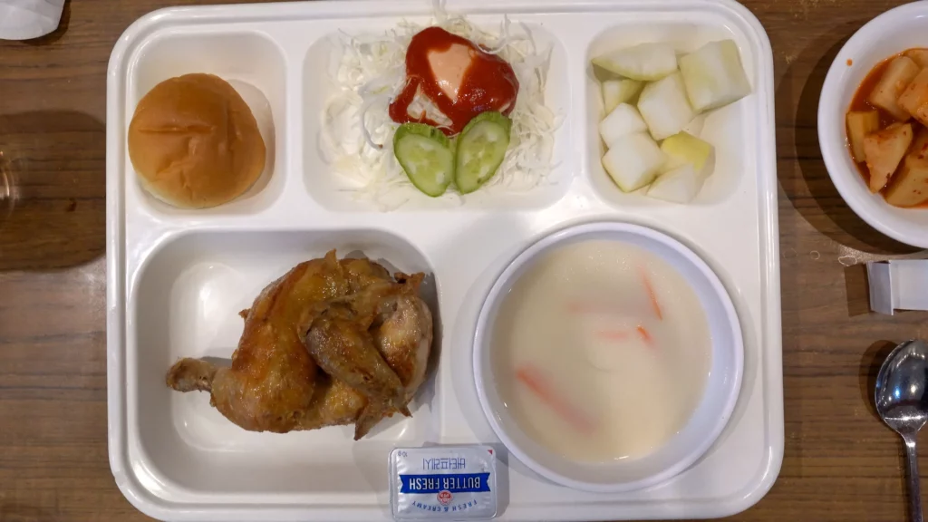 Overhead view of Yeongyang Center Myeongdong tongdak lunch set with chicken, bread roll, salad, cream soup, and pickled radish