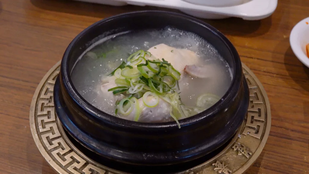 Steaming bowl of samgyetang served in a black stone pot at Yeongyang Center Myeongdong, topped with sliced green onions.
