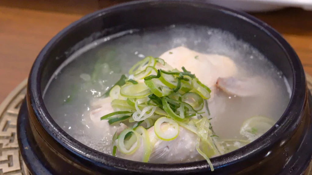 Close-up of samgyetang in a stone bowl at Yeongyang Center Myeongdong, showing tender chicken in clear ginseng broth with scallions