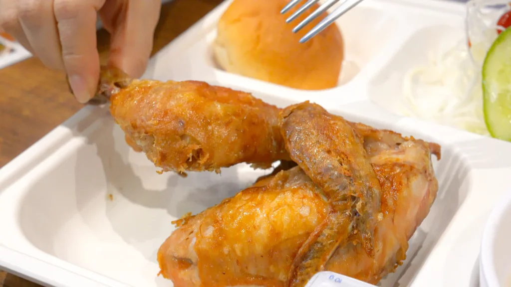 Hand lifting a crispy roasted chicken leg from the Yeongyang Center Myeongdong tongdak lunch tray, showing the golden skin texture.