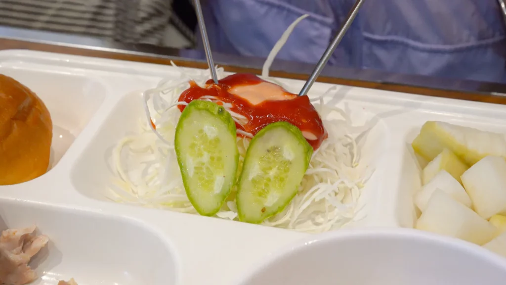 Side dish of shredded cabbage salad topped with ketchup and cucumber slices served alongside Yeongyang Center Myeongdong tongdak.