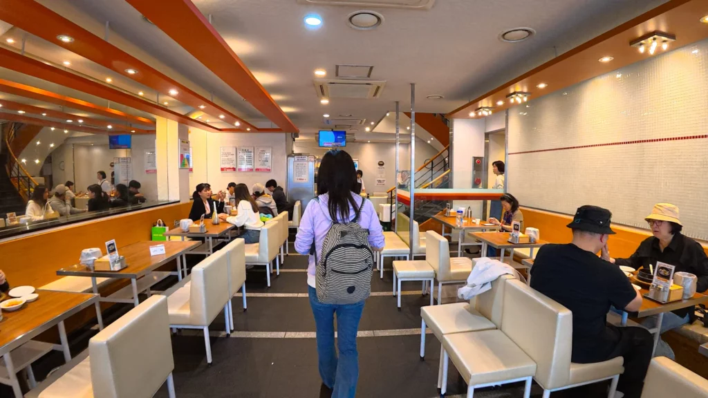Interior dining floor of Yeongyang Center Myeongdong with wooden tables, cream chairs, and customers eating tongdak and samgyetang.