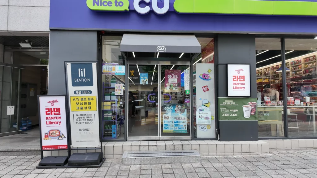 The entrance of CU Hongdae Ramyun Library with 라면 RAMYUN Library promotional signs flanking both sides of the glass door.