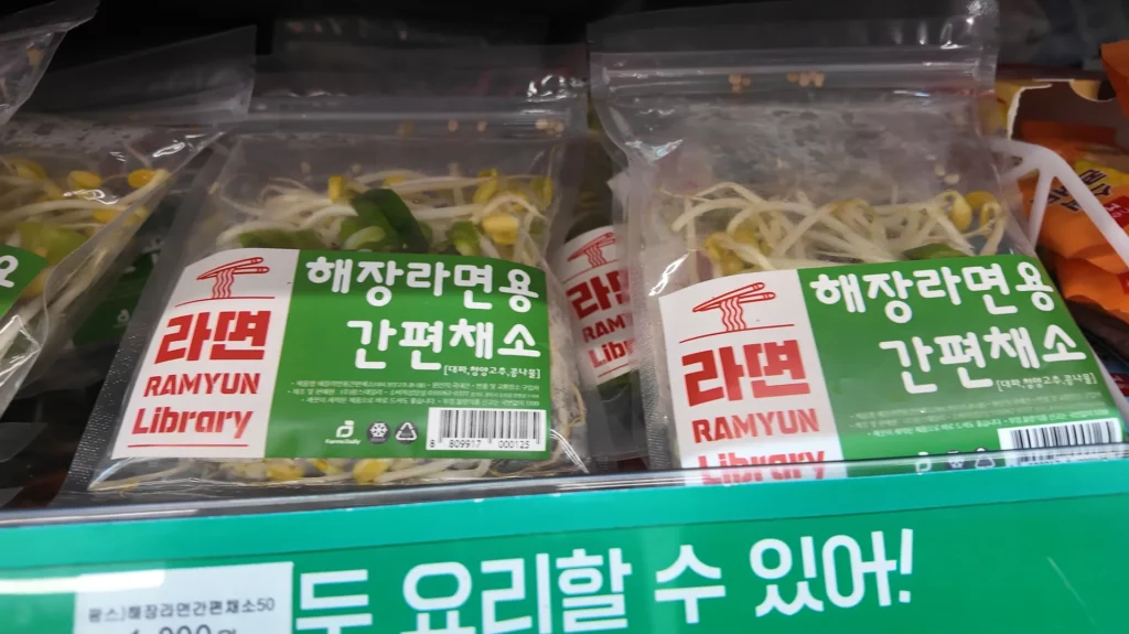 Two Ramyun Library branded 해장라면용 간편채소 (instant vegetable topping packs containing green onions, bean sprouts, and peppers) displayed in the refrigerated section of the CU store