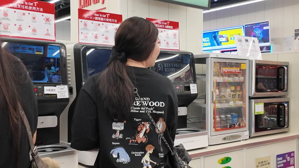A visitor operating the automated ramyun cooker machine at the CU Ramyun Library, with multilingual How To Eat instruction signs visible in the background.
