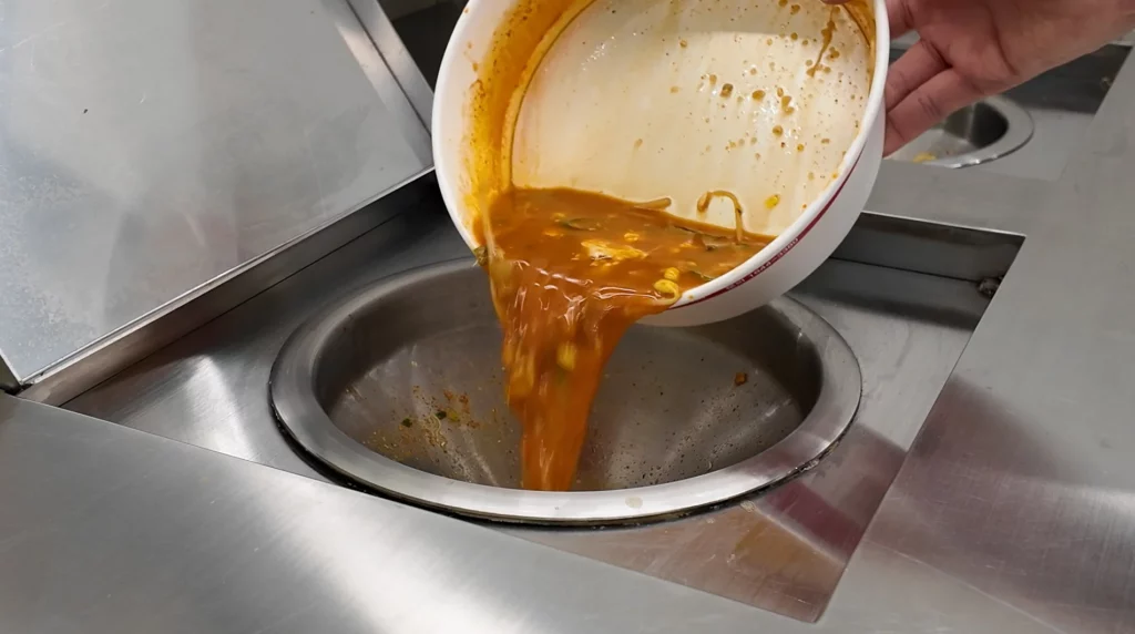 Leftover spicy orange ramyun broth being discarded into the designated drain of the CU Ramyun Library's automated cooker station after finishing a meal.