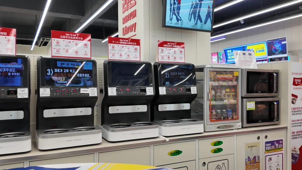 A row of automated Smart Cooker machines at the CU Ramyun Library with multilingual How To Eat instruction signs in Korean, Chinese, and Japanese mounted above each unit
